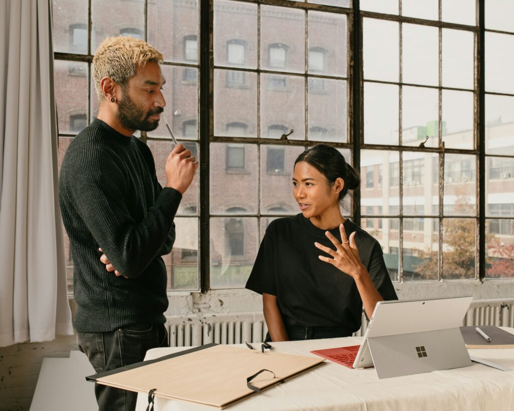 A standing manager with folded arms listening to a seated colleague during a tense workplace conversation